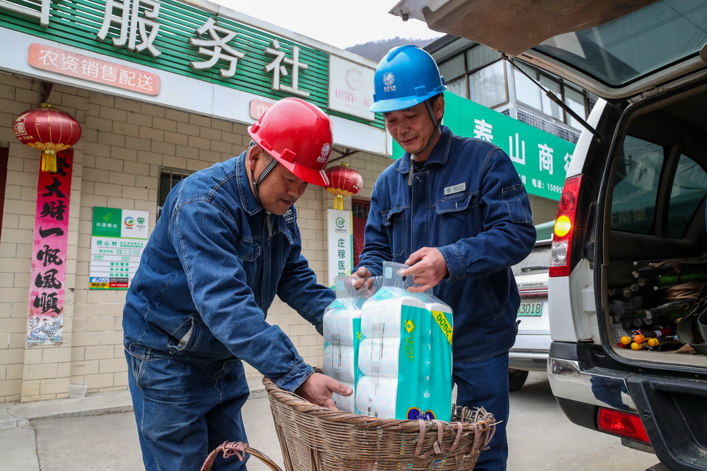 1月18日，在甘肃省陇南市两当县泰山乡同心村，杨店供电所所长宋刚（左）和工友邹小亮将代购的生活物资装进背篓，准备上山。