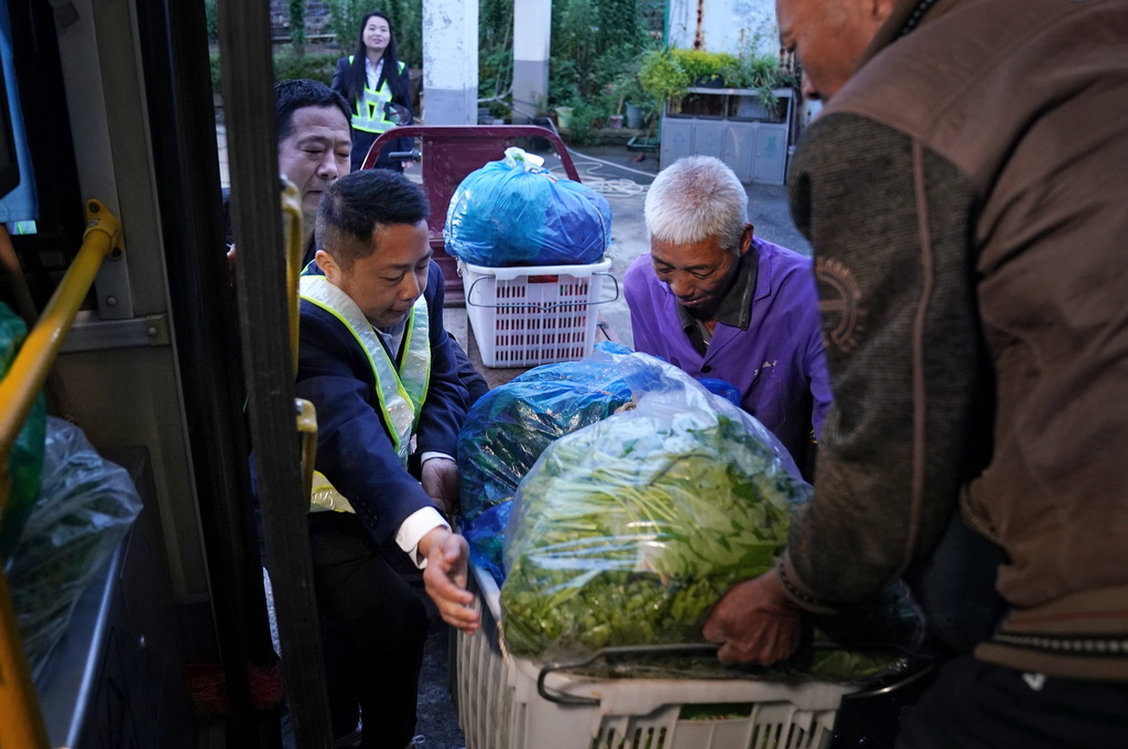 在江西省南昌县向塘镇浃溪村的公交站点,公交安全员(左前)协助年长菜农将蔬菜搬上车(5月9日摄)。