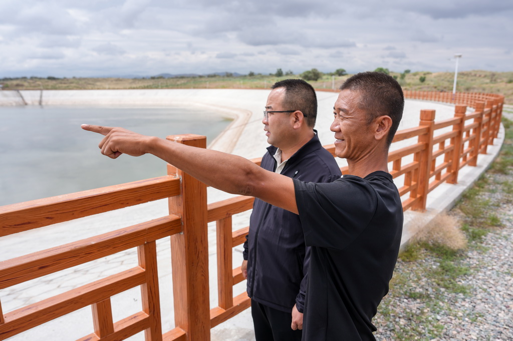 8月11日，在古浪县八步沙林场，第三代治沙人郭玺（右）与当地水务部门工作人员观察蓄水池水位。